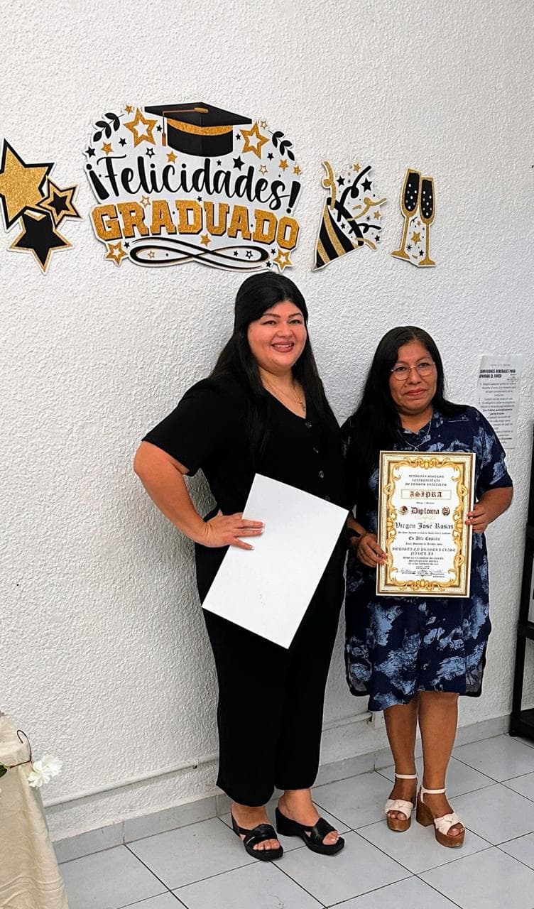 Maestra y alumna posando con su diploma en la ceremonia de graduación