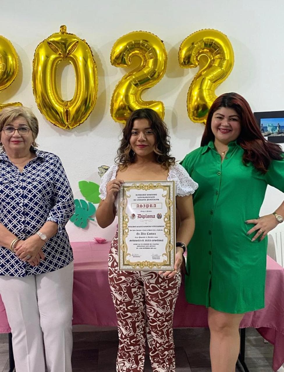 Alumna sosteniendo su diploma frente a los globos dorados de la promoción