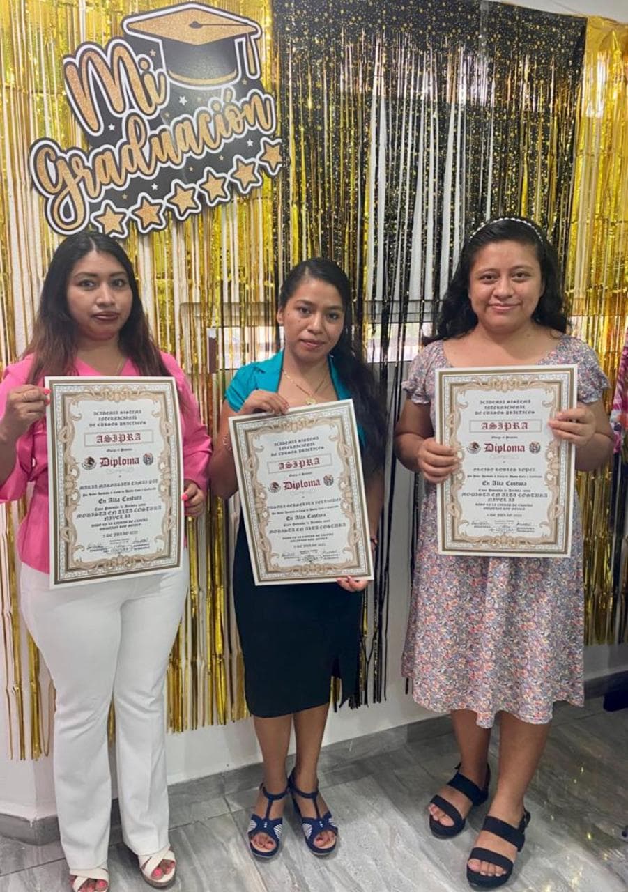 Tres alumnas sosteniendo sus diplomas con el fondo dorado de la ceremonia