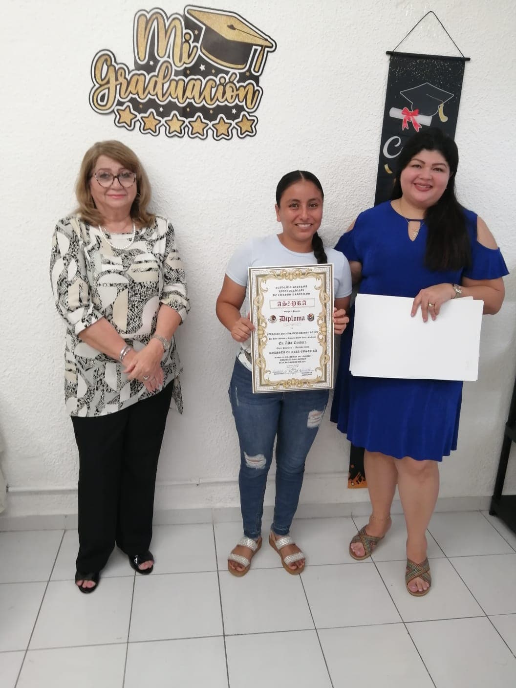 Alumna recibiendo su diploma de Alta Costura acompañada de la directora y su maestra
