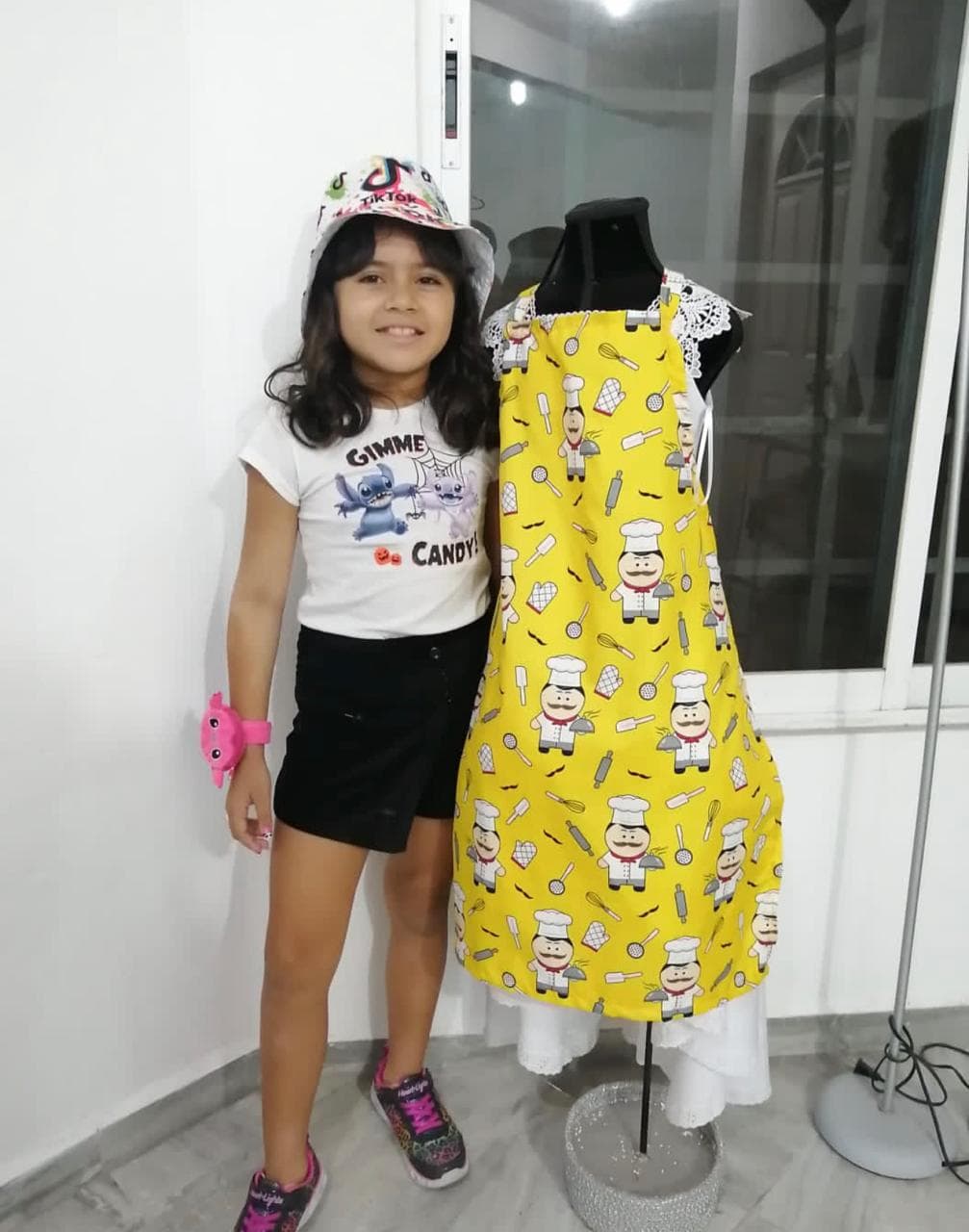 Niña posando junto a vestido infantil amarillo con estampado de chefs confeccionado en clase