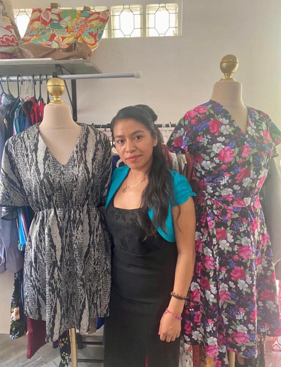 Alumna posando entre dos maniquíes con vestidos florales de su autoría